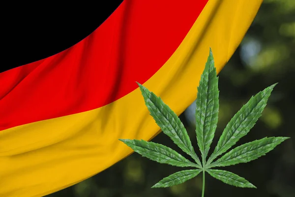 Hoja verde de cáñamo y la hermosa bandera nacional de seda de Alemania, el concepto de cannabis medicinal, la legalización de las drogas, los delitos de tráfico de drogas, primer plano — Foto de Stock