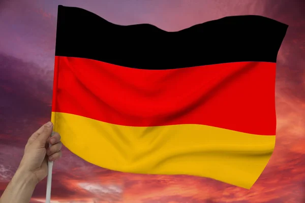 Male hand holds against the background of the sky with clouds the national flag of Germany on a luxury satin texture, silk with waves, closeup, copy space — Stock Photo, Image