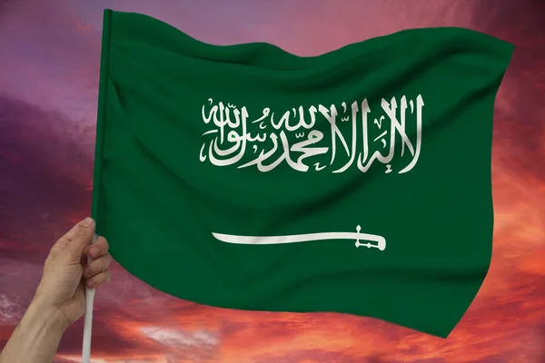 Male hand holds against the background of the sky with clouds the national flag of Saudi Arabia on a luxurious texture of satin, silk with waves, closeup, copy space, concept — Stock Photo, Image