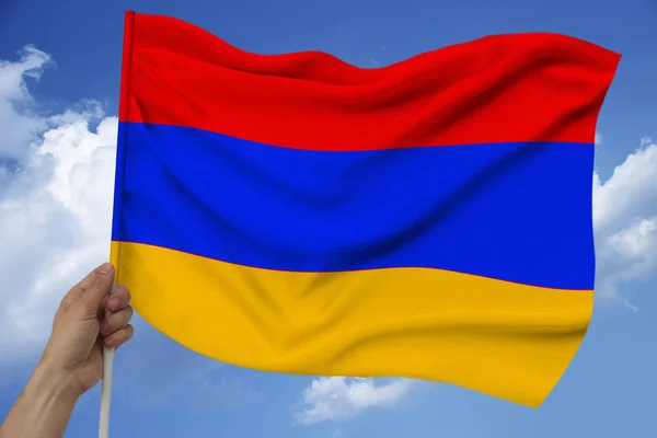 Mężczyzna trzyma rękę na tle nieba z chmur flagi narodowej Armenii na luksusową fakturę satyny, jedwabiu z falami, zbliżenie, przestrzeń kopiowania, pojęcie podróży, gospodarka, polityka — Zdjęcie stockowe