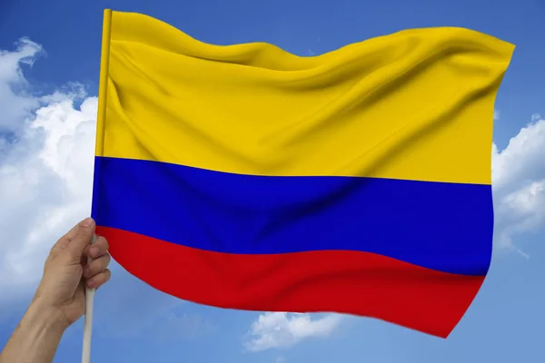 Мужская рука держит на фоне неба с облаками национальный флаг Колумбии на роскошной атласной текстуре, шелк с волнами, крупным планом, копировальное пространство, концепция путешествий, экономика, политика — стоковое фото