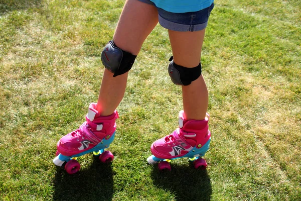 little girl riding pink four-wheeled roller skates on the grass, knee pads, legs, close-up