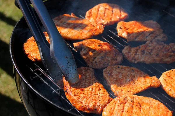 Leckere Fleisch gegrillte Steaks mit einer Zange auf der Straße auf einem schwarzen Metallgrill auf brennender Holzkohle umgekippt, Picknick-Konzept, Nahaufnahme — Stockfoto