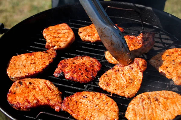 Leckere Fleisch gegrillte Steaks mit einer Zange auf der Straße auf einem schwarzen Metallgrill auf brennender Holzkohle umgekippt, Picknick-Konzept, Nahaufnahme — Stockfoto