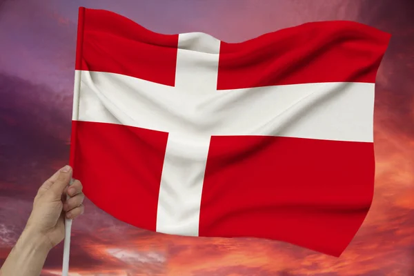 Main masculine tient le drapeau du Danemark sur le fond du ciel avec des nuages un drapeau coloré du Danemark sur une texture luxueuse de satin, soie avec des vagues, gros plan, espace de copie — Photo