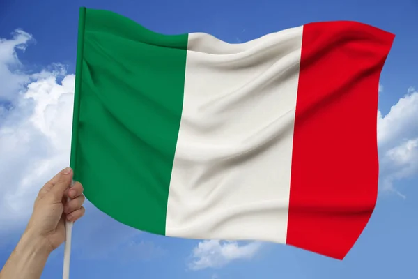 Hand holds against the background of the sky with clouds the colored flag of Italy on the texture of the fabric, silk with waves, close-up — Stock Photo, Image