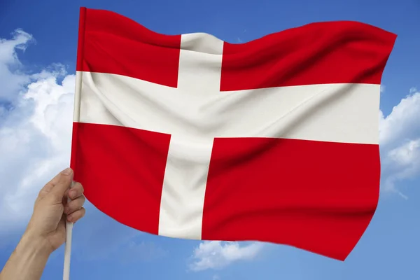 Main masculine tient le drapeau du Danemark sur le fond du ciel avec des nuages un drapeau coloré du Danemark sur une texture luxueuse de satin, soie avec des vagues, gros plan, espace de copie — Photo