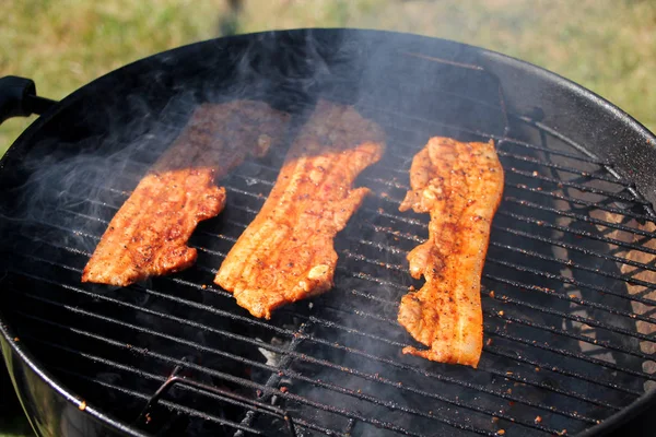 Schön gebratener, rosiger gegrillter Speck, der auf der Straße auf einem schwarzen Metallgrill auf brennenden Kohlen gebraten wird, Picknickkonzept, Nahaufnahme — Stockfoto