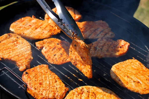 Leckere Fleisch gegrillte Steaks mit einer Zange auf der Straße auf einem schwarzen Metallgrill auf brennender Holzkohle umgekippt, Picknick-Konzept, Nahaufnahme — Stockfoto