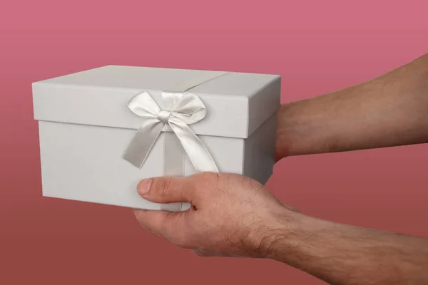 Man met een geschenk in een lichtgrijze doos met een satijnen lint en een strik, het concept van Valentijnsdag, Kerstcadeaus, Moederdag, Nieuwjaar, close-up, kopieer ruimte — Stockfoto