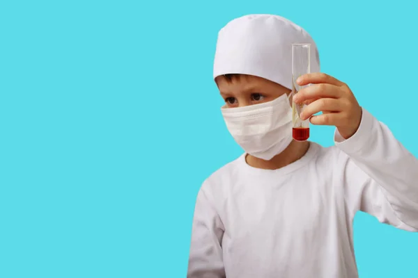 Niño en un traje médico blanco sostiene un tubo de ensayo de laboratorio de vidrio en sus manos, aislar —  Fotos de Stock