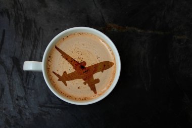 siyah bir arka plan üzerinde bir uçak silueti şeklinde cappuccino ve köpük ile beyaz fincan, üst görünüm, yakın çekim, kopya alanı