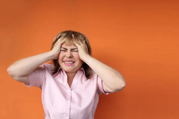 Mujer europea de mediana edad sosteniendo su cabeza, fondo naranja, dolor de cabeza concepto, estrés, primer plano, espacio de copia —  Fotos de Stock