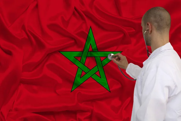 Photographie partielle d'un médecin avec un stéthoscope en uniforme médical professionnel sur fond du drapeau national de l'Etat du Maroc, concept de soins de santé, activités de l'organisation — Photo