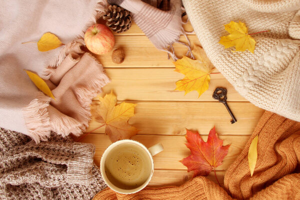 cup of hot aromatic coffee, autumn leaves, apple, cozy scarves and knitted sweaters, flat, concept of hugg, winter or autumn mood