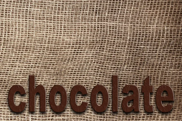 Word chocolate on a background of natural canvas, burlap with a large weave, background and texture, close-up, copy space — ストック写真