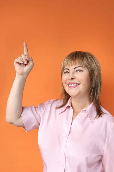 Middelbare leeftijd Europese vrouw staande, tonen boven, oranje achtergrond, close-up, kopieer ruimte — Stockfoto