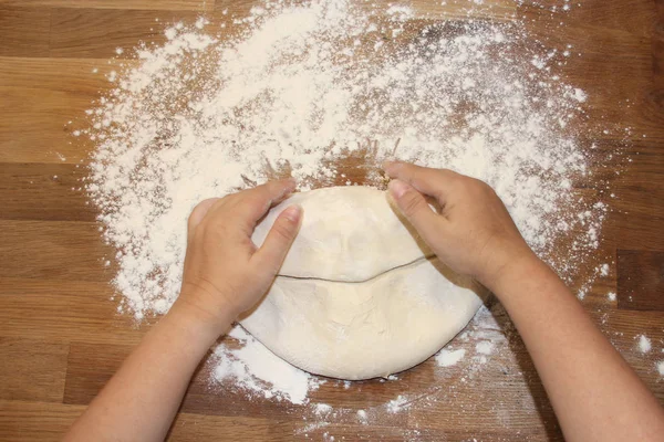 Female hands knead the dough on a wooden table, sprinkled with flour, close-up, selective focus, home cooking concept, copy space — Stock Photo, Image