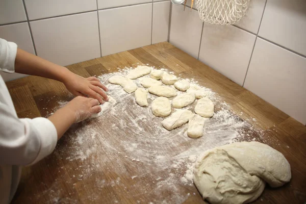 Niño esculpe productos de harina de masa en una mesa de madera, espolvoreado con harina, primer plano, enfoque selectivo, concepto de cocina en casa, espacio para copiar — Foto de Stock