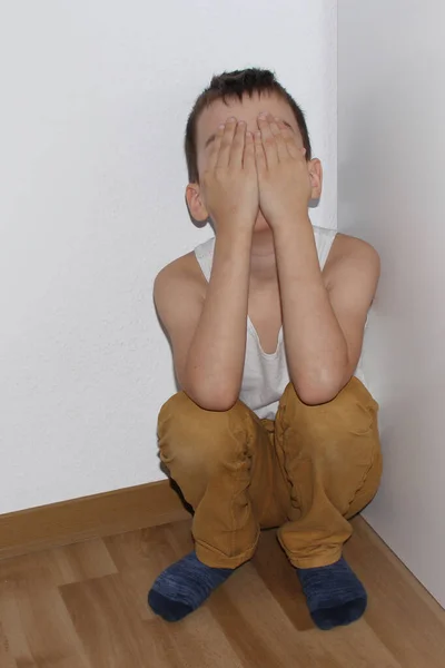 Προσβεβλημένο αγόρι κάθεται στη γωνία, ντροπή καλύπτει το πρόσωπό του με τα χέρια του, παιδαγωγική έννοια — Φωτογραφία Αρχείου