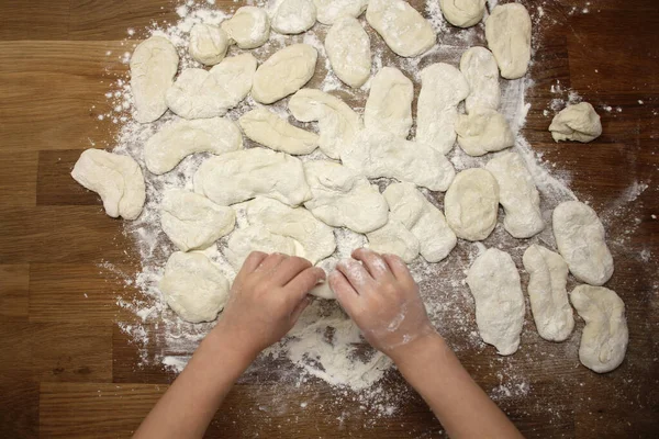 子供は木のテーブルの上に生地から小麦粉製品を彫刻し、小麦粉を振りかけ、クローズアップし、選択的な焦点を当て、家庭料理のコンセプト、コピースペース — ストック写真