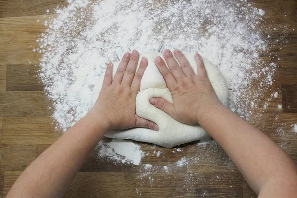 Kobiece dłonie ugniatają ciasto na drewnianym stole, posypane mąką, zbliżeniem, selektywnym ukierunkowaniem, koncepcją domowego gotowania, przestrzenią do kopiowania — Zdjęcie stockowe