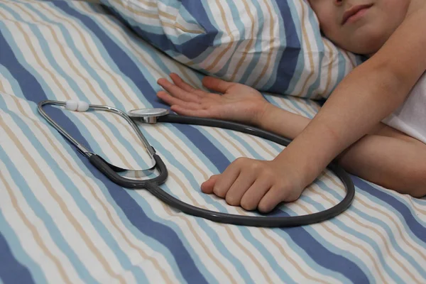 Medicinteknisk utrustning för att lyssna på ett stetoskop, begreppet medicinsk forskning och hälsovård, ligger på en säng bredvid ett barns hand, närbild, kopiera utrymme — Stockfoto