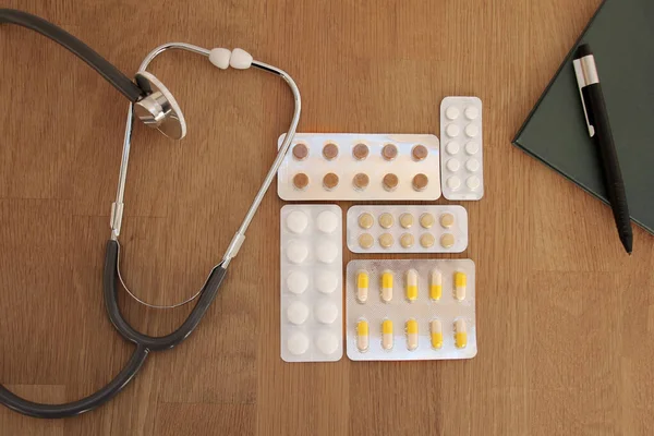 Pilulky v blistrech, lékařský stetoskop na dřevěném stole, výhled shora, zblízka, kopírovací prostor — Stock fotografie