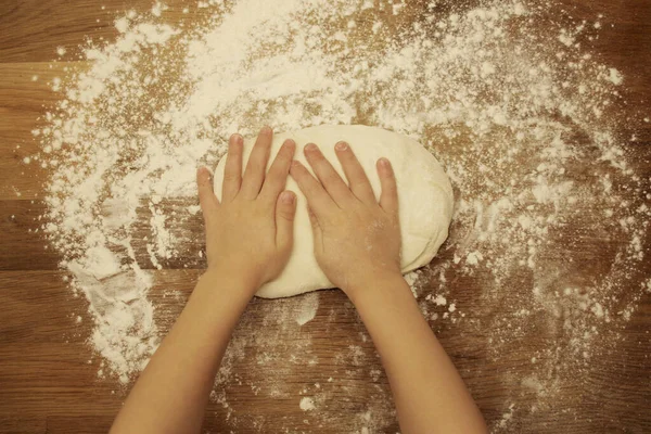Dłonie dzieci ugniatają ciasto na drewnianym stole, posypane mąką, zbliżeniem, selektywnym ukierunkowaniem, koncepcją domowego gotowania, przestrzenią do kopiowania — Zdjęcie stockowe