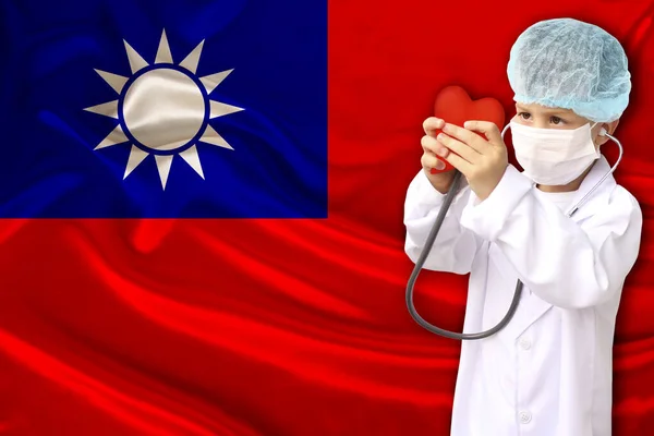 Foto di un bambino in uniforme professionale con un cuore tra le mani sullo sfondo della bandiera nazionale della Repubblica di Taiwan, il concetto di pediatria, chirurgia, cardiologia — Foto Stock