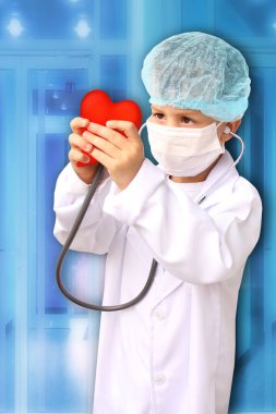 Beyaz doktor önlüklü, şapkalı ve maskeli bir çocuk kırmızı kalp modeline steteskop takmış, arka plan kliniğine yakın plan, yüze odaklanma, tıbbi konsept, kardiyoloji.