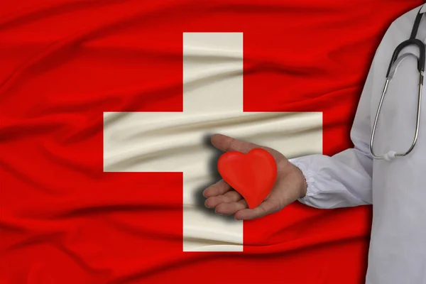 photo of a doctor with a stethoscope with a heart in his hand against the background of the national flag of the state of Switzerland, the concept of health care, cardiological treatment, medical insu