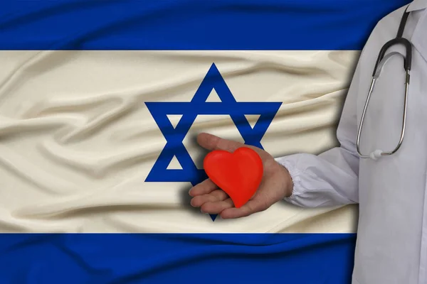 Foto van een arts met een stethoscoop met een hart in de hand tegen de achtergrond van de nationale vlag van Israël, het concept van de gezondheidszorg, cardiologische behandeling, ziektekostenverzekering — Stockfoto