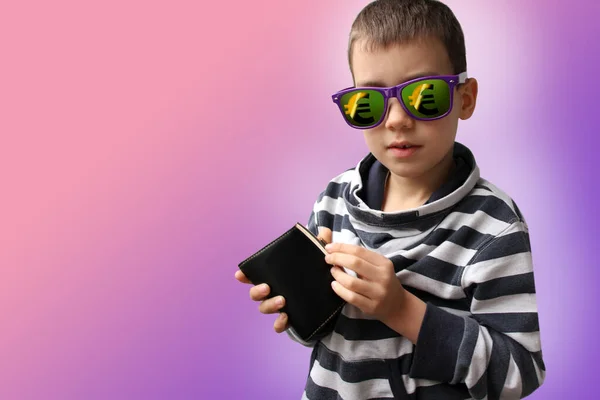 Niño en gafas de sol oscuras, cuyo reflejo muestra el signo del euro, en un suéter a rayas, abre una cartera de cuero negro, espacio para copiar, coral, fondo púrpura, primer plano — Foto de Stock