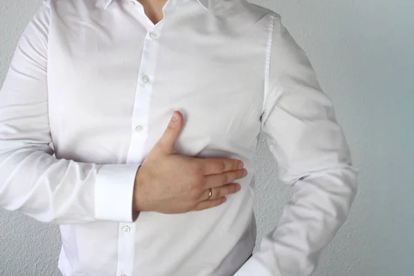 Hombre con una camisa blanca se aferra al pecho en el corazón, símbolo de problemas, dolor, enfermedad, primeros auxilios, primer plano — Foto de Stock