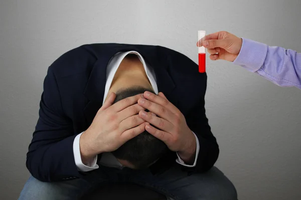 Mano di un assistente di laboratorio tiene una provetta con sangue, liquido rosso, un uomo d'affari siede con la testa tra le mani, simbolo di problemi, dolore, malattia, primo piano, spazio copia — Foto Stock