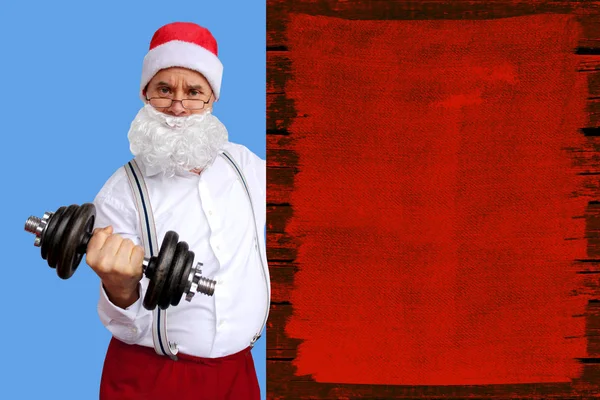 Santa Claus with glasses, in a white shirt, pumps his muscles with dumbbells, peeking out from behind a red grunge wall, Christmas and sports concept, close-up
