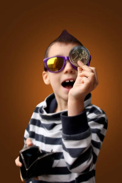 Menino com um mohawk na cabeça, em óculos escuros mostra entusiasticamente uma grande moeda de metal de 2 euros, conceito de negócio, close-up — Fotografia de Stock