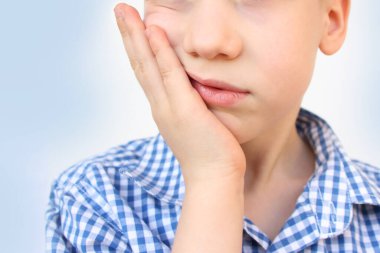 Evlat, bir okul çocuğu elini alt çenesinde tutar, diş ağrısı kırışıklıkları, pediatrik dişçilik konsepti, süt dişlerinin tedavisi, ağız bakımı