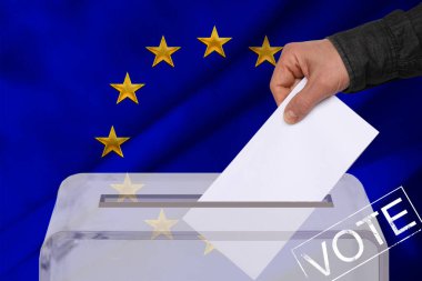 Erkek seçmen, AB ulusal bayrağı, devlet seçimleri konsepti ve referandumun arka planına karşı şeffaf bir oy sandığında oyunu düşürdü