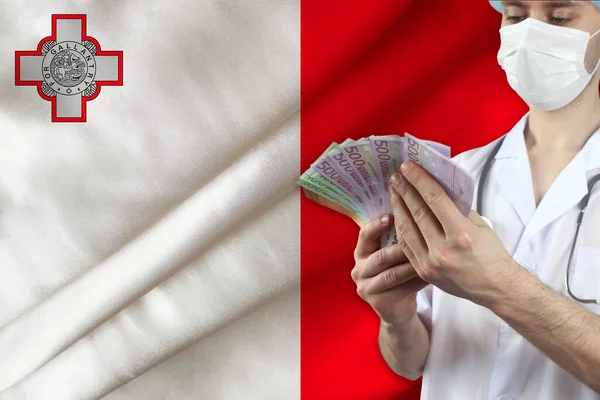 doctor with a stethoscope holds euro banknotes in the background of the silk national flag of Malta, the concept of medical insurance, budget, cost of treatment, organ donation