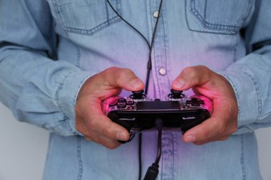 Adam elinde modern bir oyun konsolu için mor arkaplan ışığı olan siyah bir oyun sahası tutuyor. Bilgisayar oyunları konsepti, kumar bağımlılığı, hobiler.