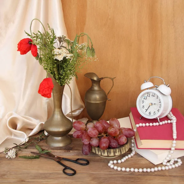 古い木製のテーブルの上の古い真鍮のジャグの野生の花 赤いケシ 目覚まし時計 ブドウ シルクのドレープ 時間の概念 オランダの静物画 — ストック写真
