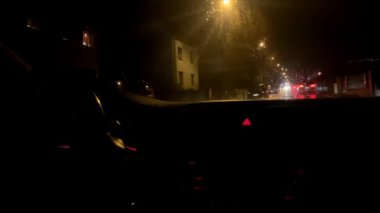 Araba gece vakti bir Avrupa şehrinde yağmurda araba sürüyor, damlalar ıslak camların üzerine düşüyor, seyahat konsepti, gece çalışıyor, trafik, bulanık görüntü