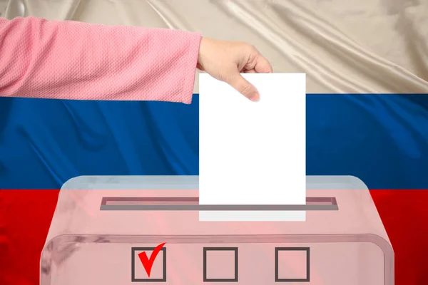 woman voter lowers the ballot in a transparent ballot box on the background of the national flag of Russia concept of state elections, referendum