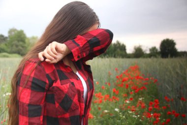 Kırmızı gelinciklerin açtığı bir tarlada ağlayan, gömleğinin koluyla gözyaşlarını silen, mutsuzluk konsepti, aşkta hayal kırıklığı, psikolojik sorunlar, gaz lambası...