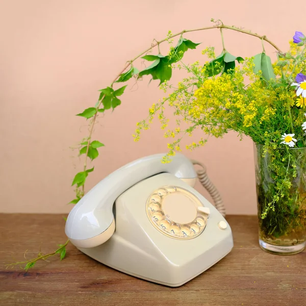 木製のテーブルの上には シンプルな野の花の花束とガラスの花瓶 古い電話 夏の気分の概念 古い通信技術 — ストック写真