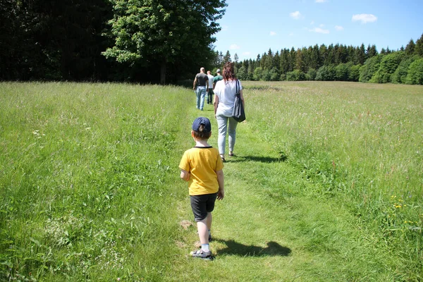 child is behind a large group of people, families of three generations walk along the path among meadows and forests in the summer, concept of family summer vacations, lost, going to forest, park