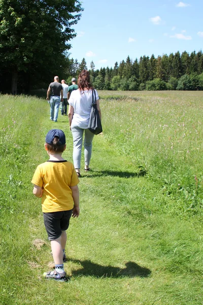 child is behind a large group of people, families of three generations walk along the path among meadows and forests in the summer, the concept of family summer vacations, lost, going to forest, park