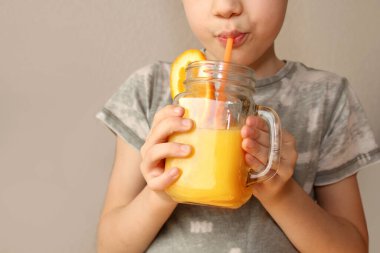 Neşeli çocuk elinde portakal suyu ve limonla dolu bir kavanoz tutuyor ve pipetten içiyor. Sağlıklı beslenme, vitamin, yaşam tarzı...